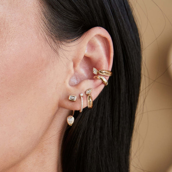 close up of a woman's ear wearing a Zoë Chicco 14k Gold Marquise Diamond Chubby Ear Cuff layered with another ear cuff and a Marquise Diamond Bezel Chubby Huggie Hoops