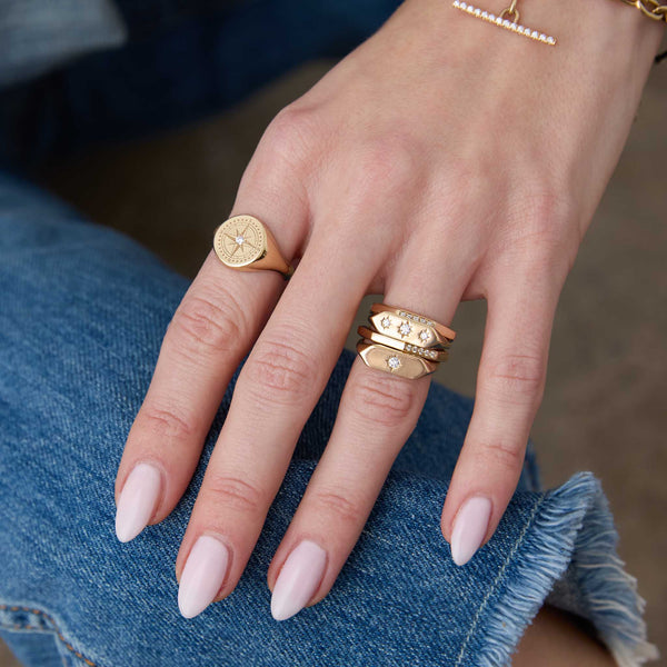 woman's hand wearing a Zoë Chicco 14k Gold Diamond Compass Signet Ring on her index finger along with a 14k Star Set Diamond Elongated Hexagon Signet Ring, 14k Graduated Star Set Diamonds Elongated Hexagon Signet Ring, and 2 14k Pavé Diamond Octagon Rings stacked on her ring finger
