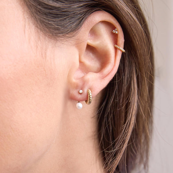 close up of a woman's ear wearing a Zoë Chicco 14k Gold Diamond Stud with Pearl Jacket Earring layered with a Gold Twisted Thick Huggie Hoop
