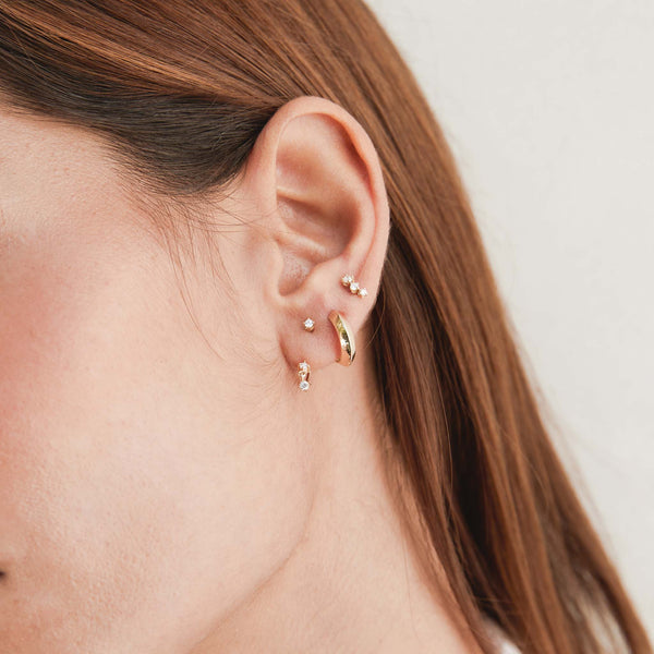 woman's ear wearing a Zoë Chicco 14k Gold Knife Edge Hinge Huggie Hoop Earring in her second piercing layered with two diamond earrings