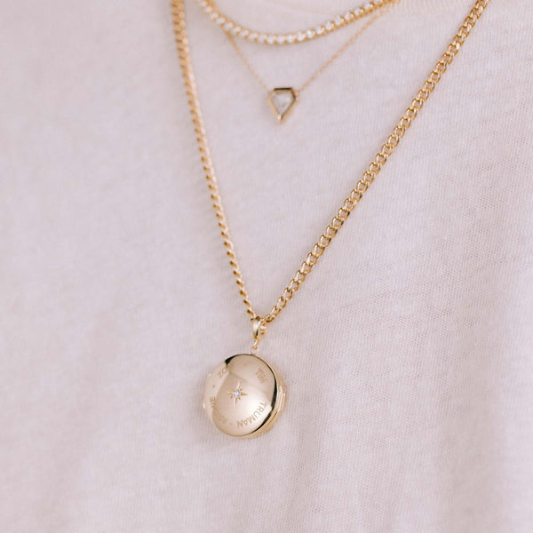 close up of a Zoë Chicco 14k Gold Family Names Round Locket Necklace against a white tshirt