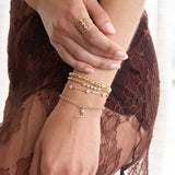 Zoe Chicco 14k gold bracelets on a hand with a dark red lace garment background