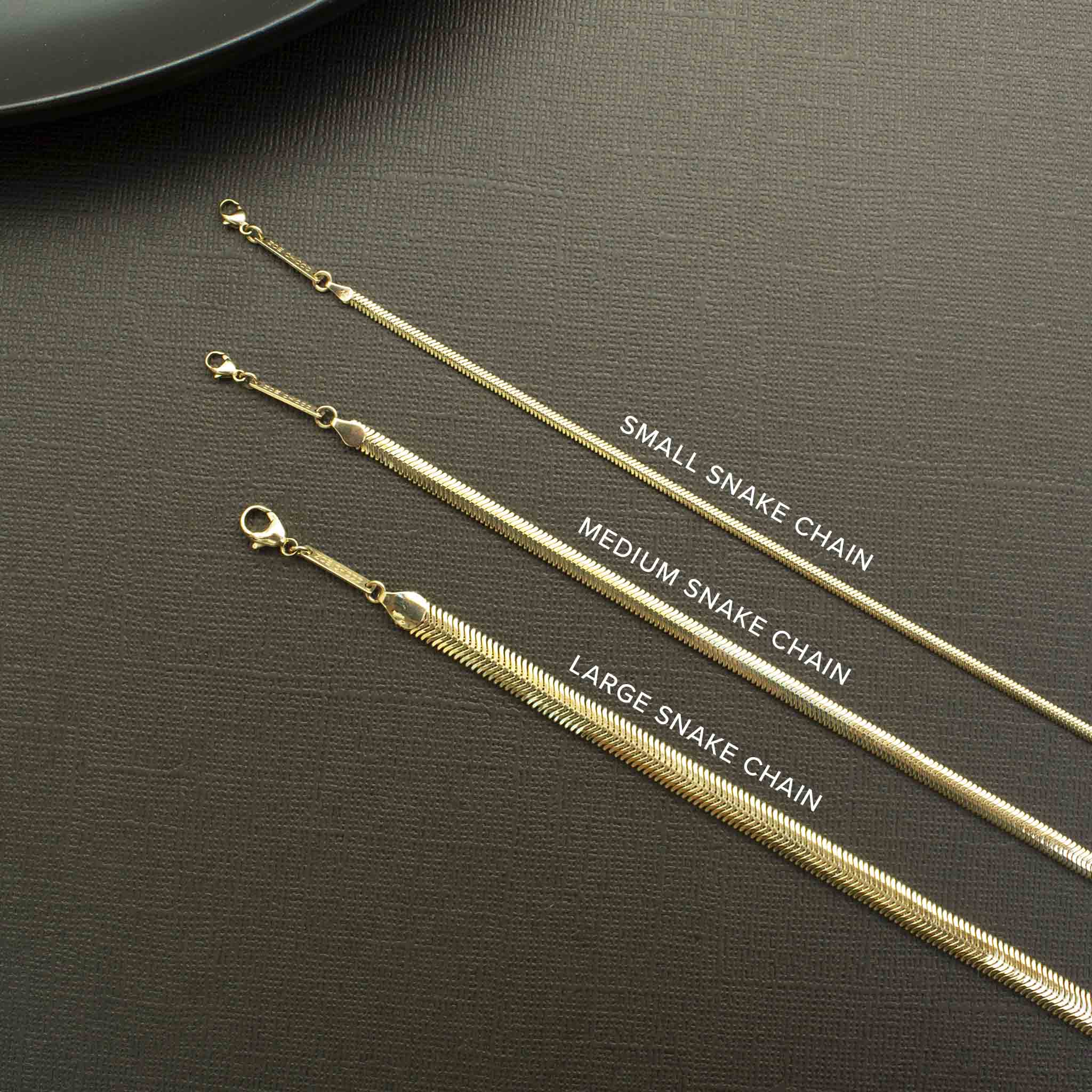 3 Zoë Chicco 14k Gold Snake Chains in different widths laying flat against a black background to compare sizes