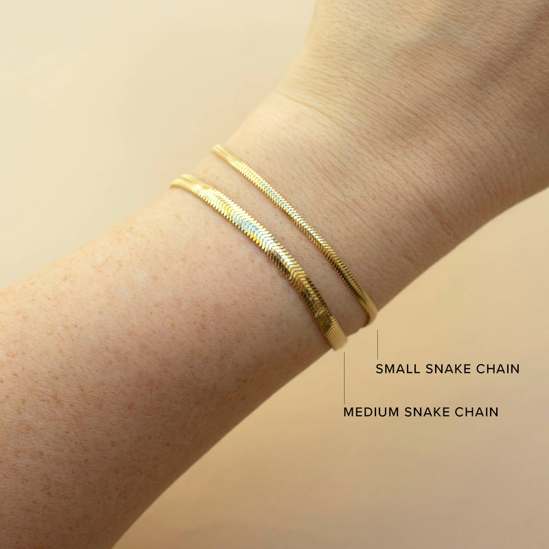 a woman's wrist against a beige background wearing a Zoë Chicco 14k Gold Small Snake Chain Bracelet stacked with a Medium Snake Chain Bracelet to compare sizes