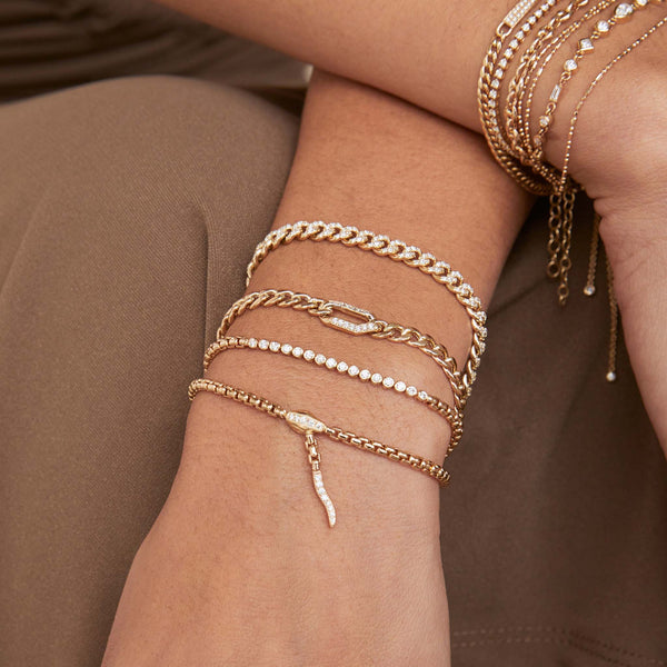 close up of a woman's wrist laying on her lap wearing a Zoë Chicco 14k Gold Small Diamond Bezel Tennis Segment Box Chain Bracelet layered with three other bracelets