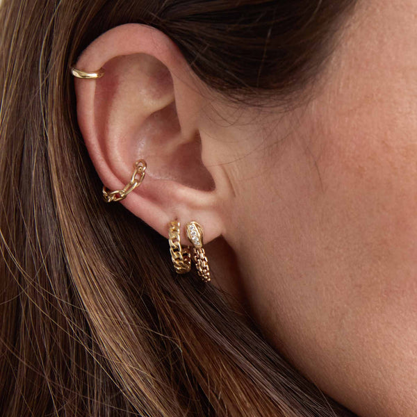 close up of a brunette woman's ear wearing a Zoë Chicco 14k Gold Small Curb Chain Hinge Huggie Hoop Earring in her second piercing and a 14k Pavé Diamond Snake Head Box Chain Huggie Earring in her first layered with a 14k Medium Square Oval Link Chain Ear Cuff and a XS Hinge Huggie Hoop