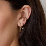 close up of a woman's ear wearing a Zoë Chicco 14k Gold Dangling Pearl Small Hinge Huggie Hoop Earring layered with a 14k Gold Safety Pin with Pearl Threader Earring and a 14k Pearl Double Wire Ear Cuff
