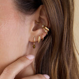 Close-up of an ear with gold earrings and a hand touching the side of the face featuring 14k Dangling Pear Tiger Eye Small Pavé Diamond Hinge Huggie Hoops