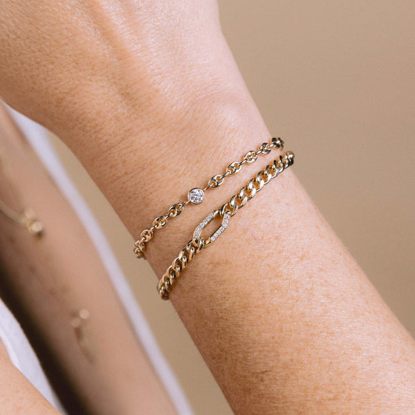 A woman is wearing the Zoë Chicco 14k Gold Floating Diamond Small Puffed Mariner Chain Bracelet and a  14k Gold Pavé Diamond Oval Link Medium Curb Chain Bracelet stacked together on her wrist