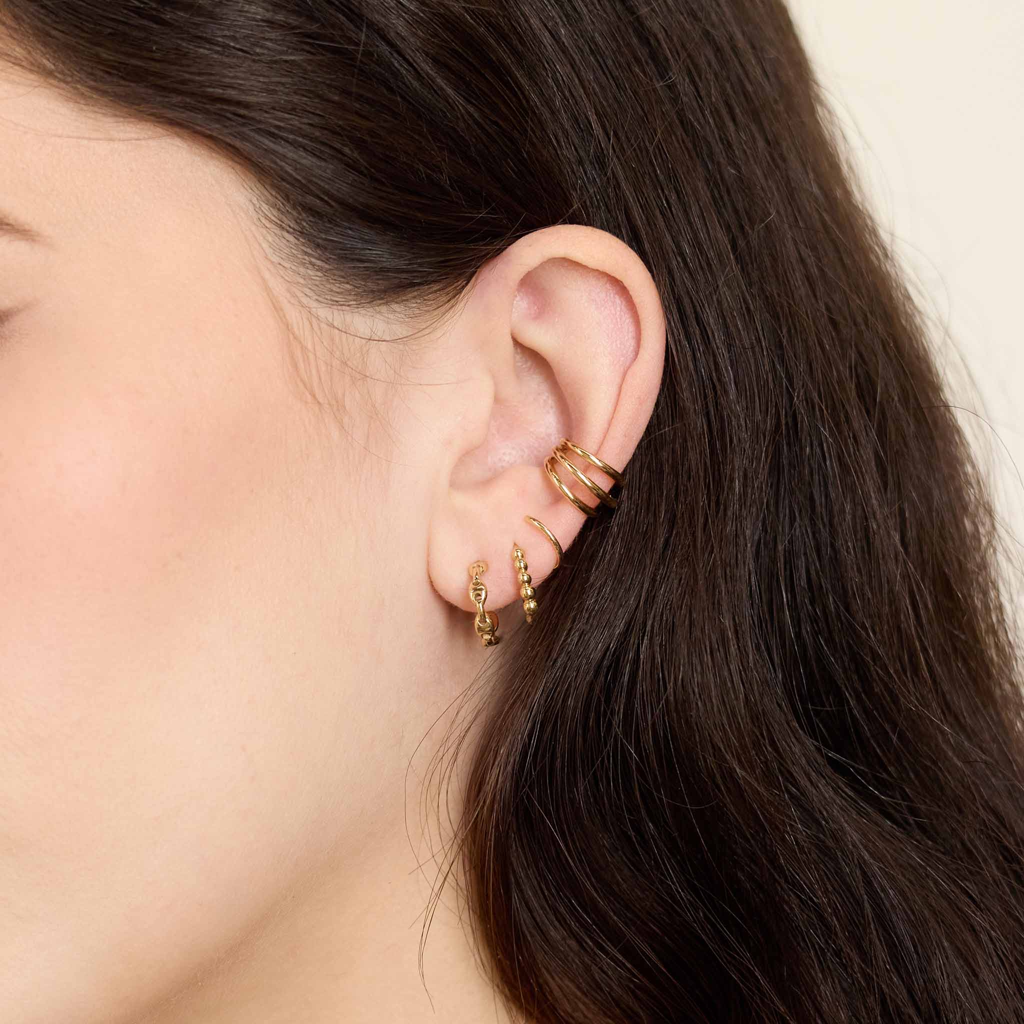 close up of a woman's ear wearing a Zoë Chicco 14k Gold Small Mariner Chain Huggie Hoop Earring layered with a Beaded Huggie and a Triple Wire Ear Cuff