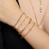 close up of a woman's wrist wearing a Zoë Chicco 14k Gold Small Mariner Station Medium Rolo Chain Bracelet stacked with a 14k 3 Diamond Quad & Linked Prong Diamond Segment Bracelet, 14k Diamond Link Large Paperclip Rolo Bracelet, and a 14k Mixed Diamond Bezel Barbell Medium Rolo Chain Bracelet