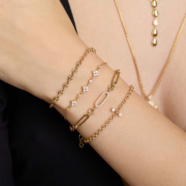 Close up of a wrist wearing multiple Zoe Chicco 14k gold chain bracelets and necklaces on a blurred background