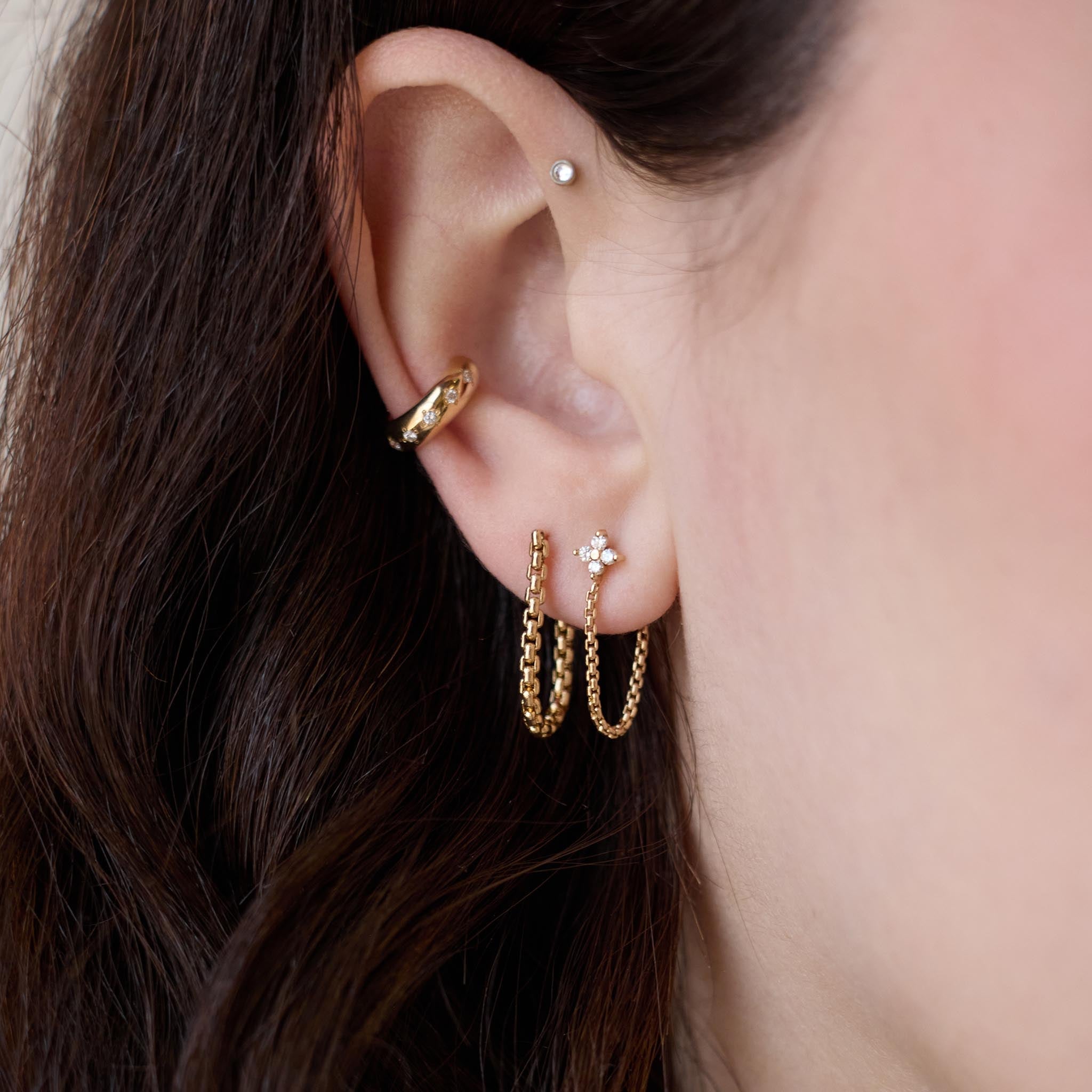 Close up of an ear wearing multiple Zoe Chicco 14k gold chain huggie hoop earrings