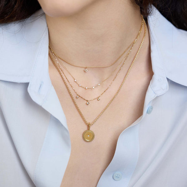 Zoe Chicco 14K Gold and diamond layered necklaces on a person wearing a blue shirt