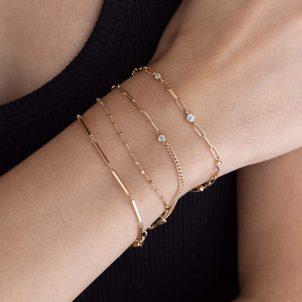 woman's wrist wearing a Zoë Chicco 14k Gold Square Bead Chain Bracelet stacked with a 14k Gold Linked Bar Bracelet, 14k Floating Diamond Mixed XS Curb & Small Paperclip Chain Bracelet, and a 14k Graduated Diamond Bezel Small Paperclip Chain Bracelet