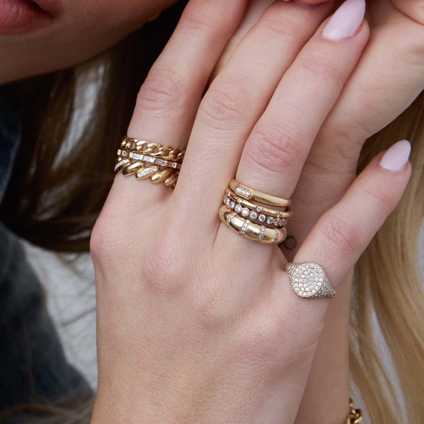 woman's hand wearing a Zoë Chicco 14k Gold 3 Diamond Hexagon Signet Ring stacked with a 14k 10 Spread Out Pavé Diamond Thick Band Ring, 14k 2mm Diamond Bezel Eternity Band Ring, 14k Pavé Diamond Banded Half Round Ring on her ring finger as well as a 14k Full Pavé Diamond Oval Signet Ring on her pinky and a 14k Pavé Diamond Line San Marco Band Ring, 14k Baguette Diamond Eternity Band, and a 14k Solid Medium Curb Chain Band Ring stacked onto her index finger