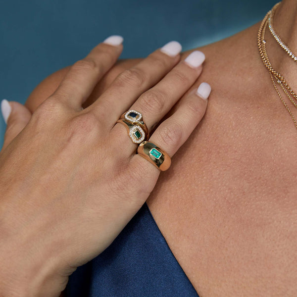 close up of woman resting her hand on her shoulder wearing a Zoë Chicco 14k Gold Emerald Cut Blue Sapphire Diamond Halo Signet Ring stacked with a Zoë Chicco 14k Gold Emerald Cut Emerald Diamond Halo Signet Ring on her ring finger