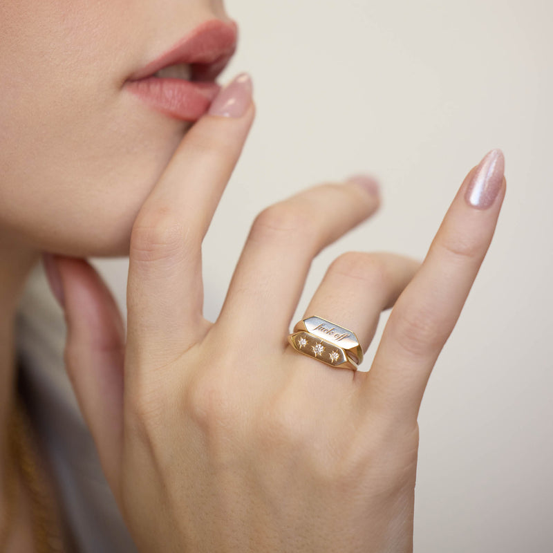 woman's hand resting against her chin wearing a Zoë Chicco 14k Gold "fuck off" Elongated Hexagon Signet Ring stacked with a 14k Graduated Star Set Diamonds Elongated Hexagon Signet Ring on her ring finger