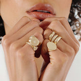 woman with her hands up to her chin wearing a Zoë Chicco 14k Gold Small Sunbeam Engraved Signet Ring stacked with other chunky rings on her pinky finger
