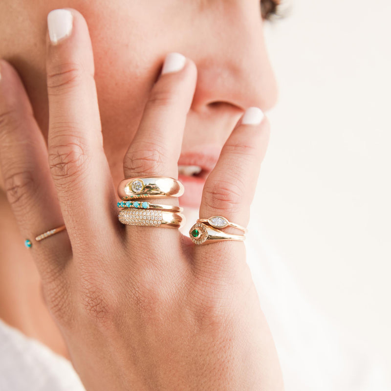 a woman's hand resting against her face wearing a Zoë Chicco 14k Gold 5 Prong Turquoise Band Ring with two other rings on her ring finger