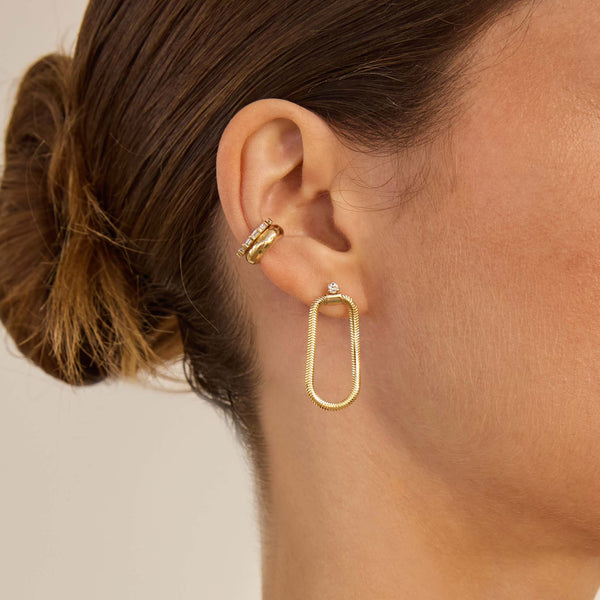 Close up of a woman wearing Zoe Chicco 14k gold earrings on a neutral background