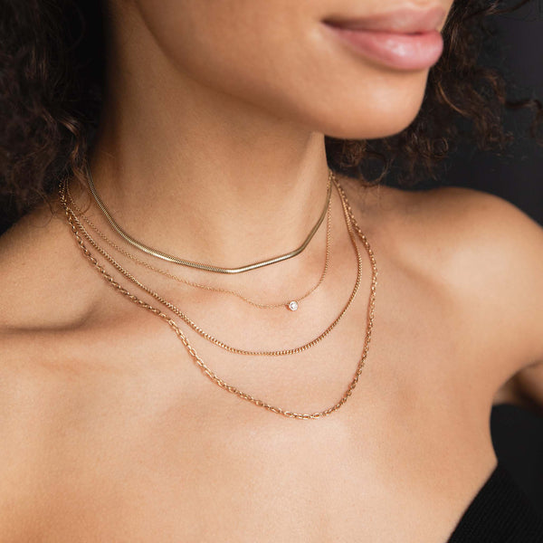 A Zoe Chicco Necklace stack including a small snake chain necklace, small floating diamond necklace and a double layer X-small curb chain and small oval link chain.