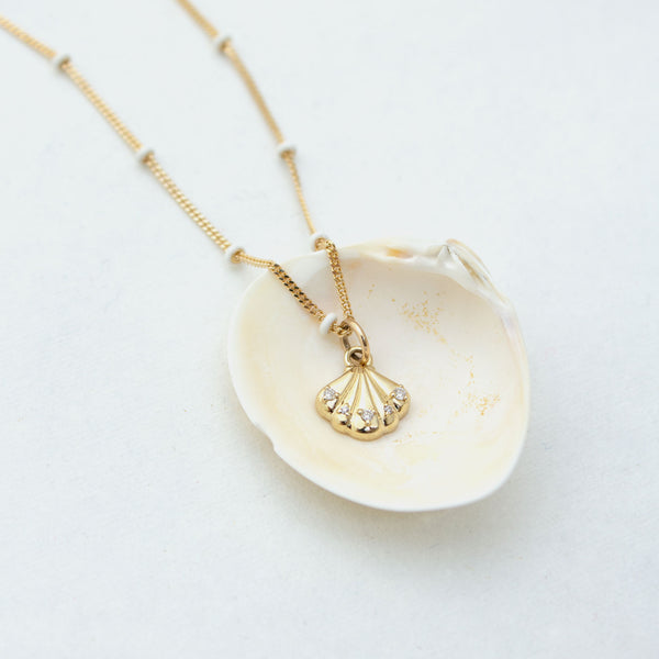 a Zoë Chicco 14k Gold and Diamond Seashell White Enamel Satellite Chain Necklace laying in a shell on a white background
