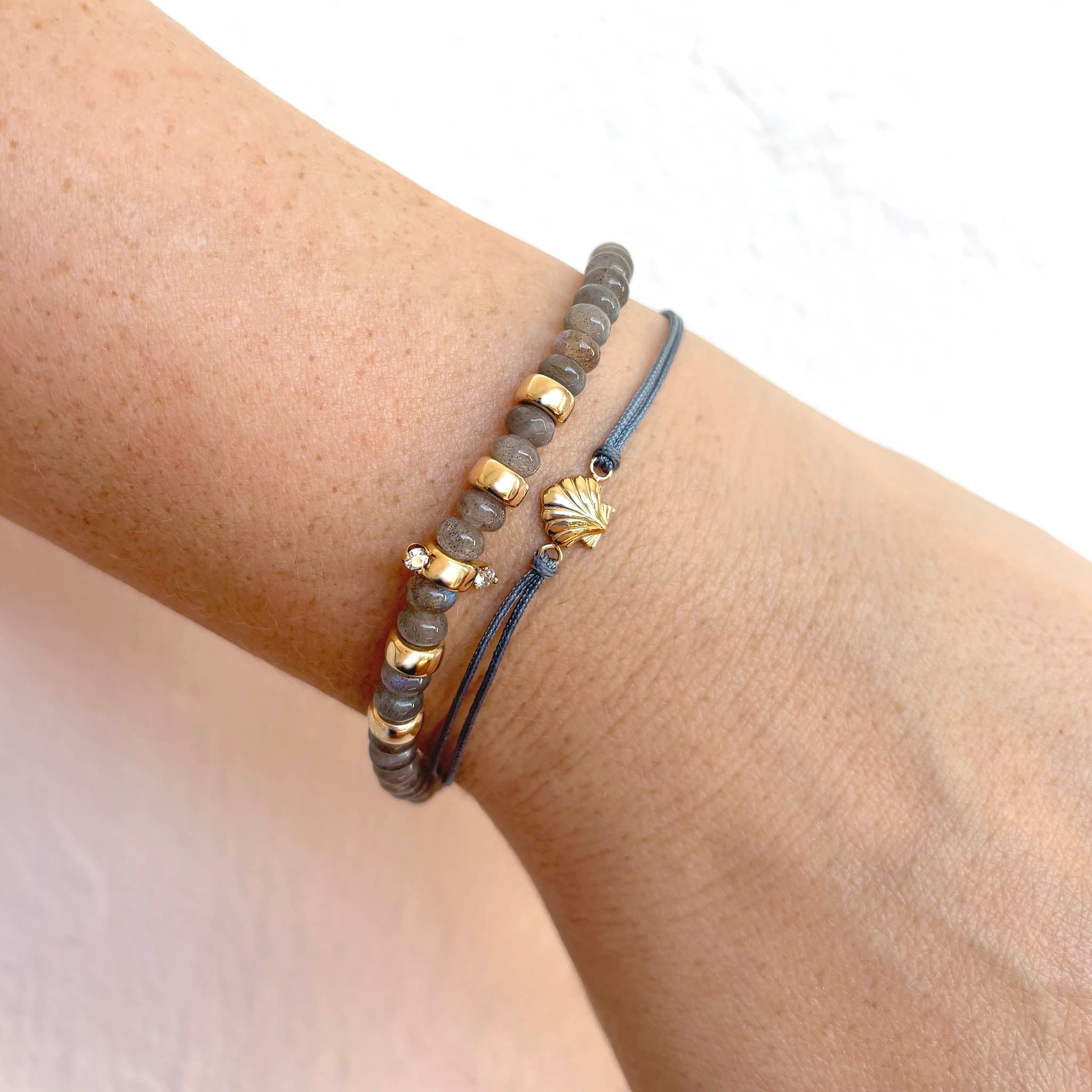Zoe Chicco's 14k Gold Seashell Thick Cord Bracelet and labradorite bead bracelet is shown on model
