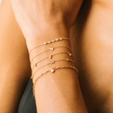 woman's wrist wearing a Zoë Chicco 14k Gold Itty Bitty Pavé Diamond Heart Padlock Bracelet layered with four other dainty bracelets