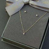 Presented on a gray is a set of diamond earrings and a solitaire diamond necklace..