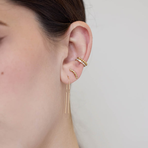 close up of a woman's ear wearing a Zoë Chicco 14k Gold Medium Beaded Curve Stud Earring in her second piercing layered with a 14k Gold U Wire Threader Earring and a Diamond Bezel Eternity Ear Cuff and Gold Beaded Ear Cuff