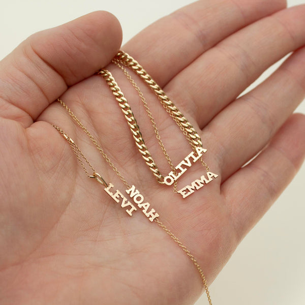 woman's hand holding various Zoë Chicco 14k Gold Custom Itty Bitty Letters jewelry pieces in her palm with different customized names