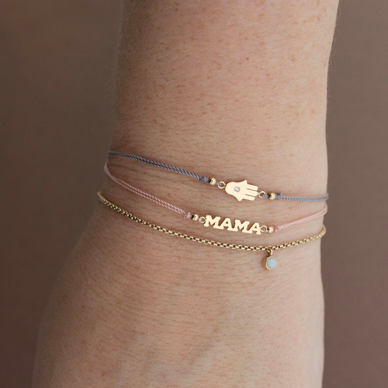 A woman's wrist is stacked with 14k Itty Bitty MAMA Cord Bracelet  and 14k Midi Bitty hamsa Cord Bracelet