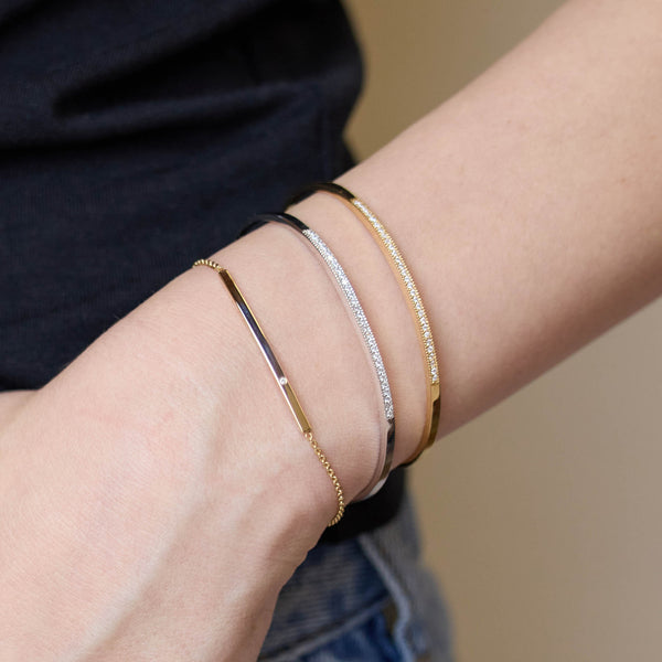 Close-up of a person's wrist wearing multiple Zoe Chicco 14k gold and silver bracelets on a neutral background