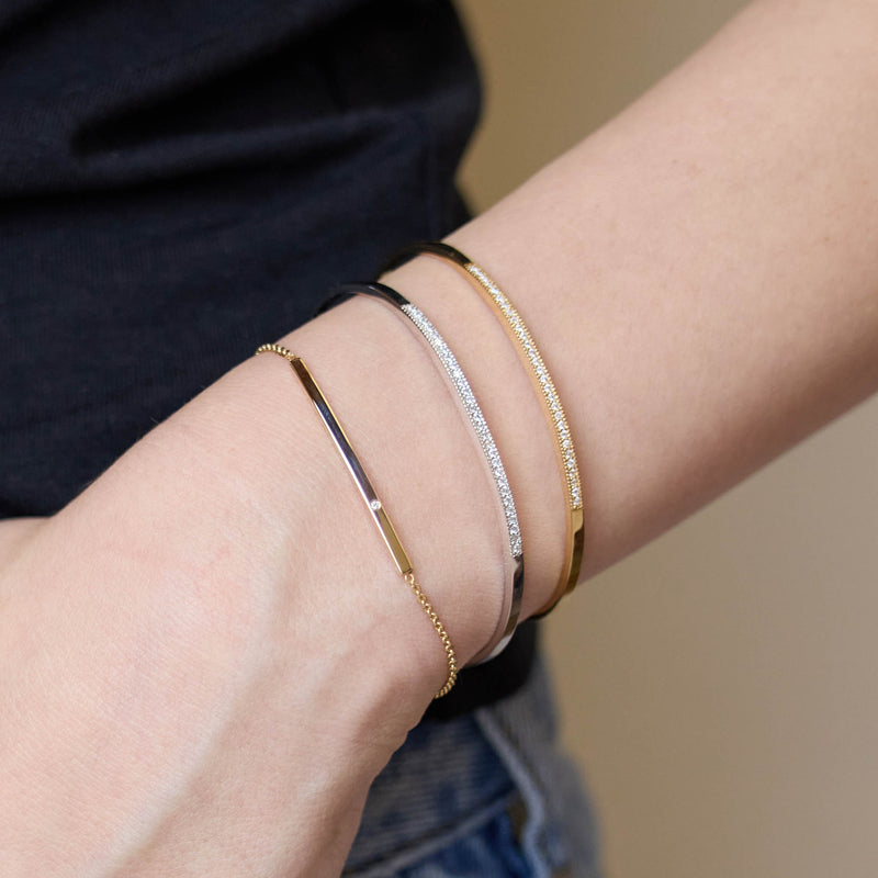 Close-up of a person's wrist wearing multiple Zoe Chicco 14k gold and silver bracelets on a neutral background