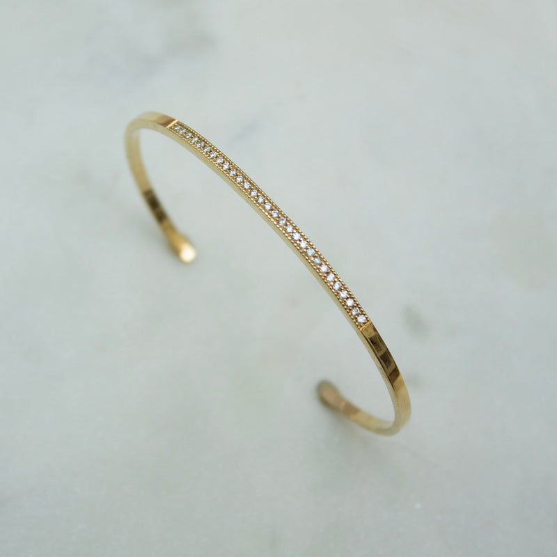 Gold cuff bracelet with pave diamonds on a light gray background