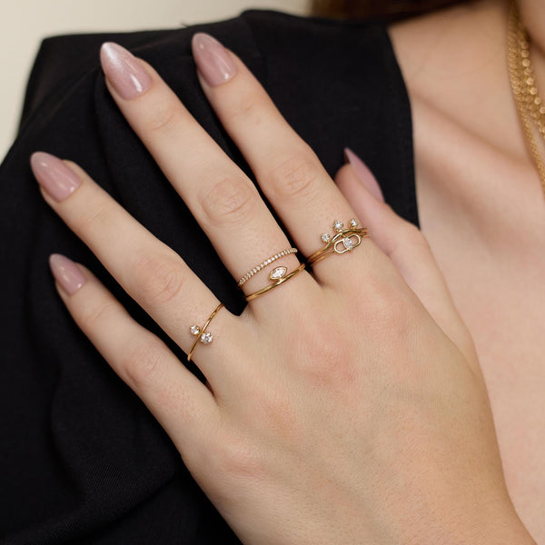 Close up of a hand wearing multiple Zoe Chicco 14k gold rings with small white diamonds with a blurred dark background