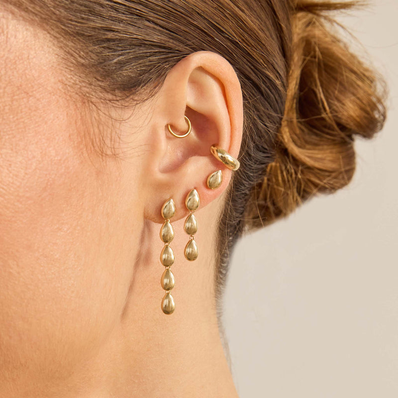 Close-up of a person wearing Zoe Chicco 14k gold hoop earrings and teardrop shaped dangling earrings with a neutral background