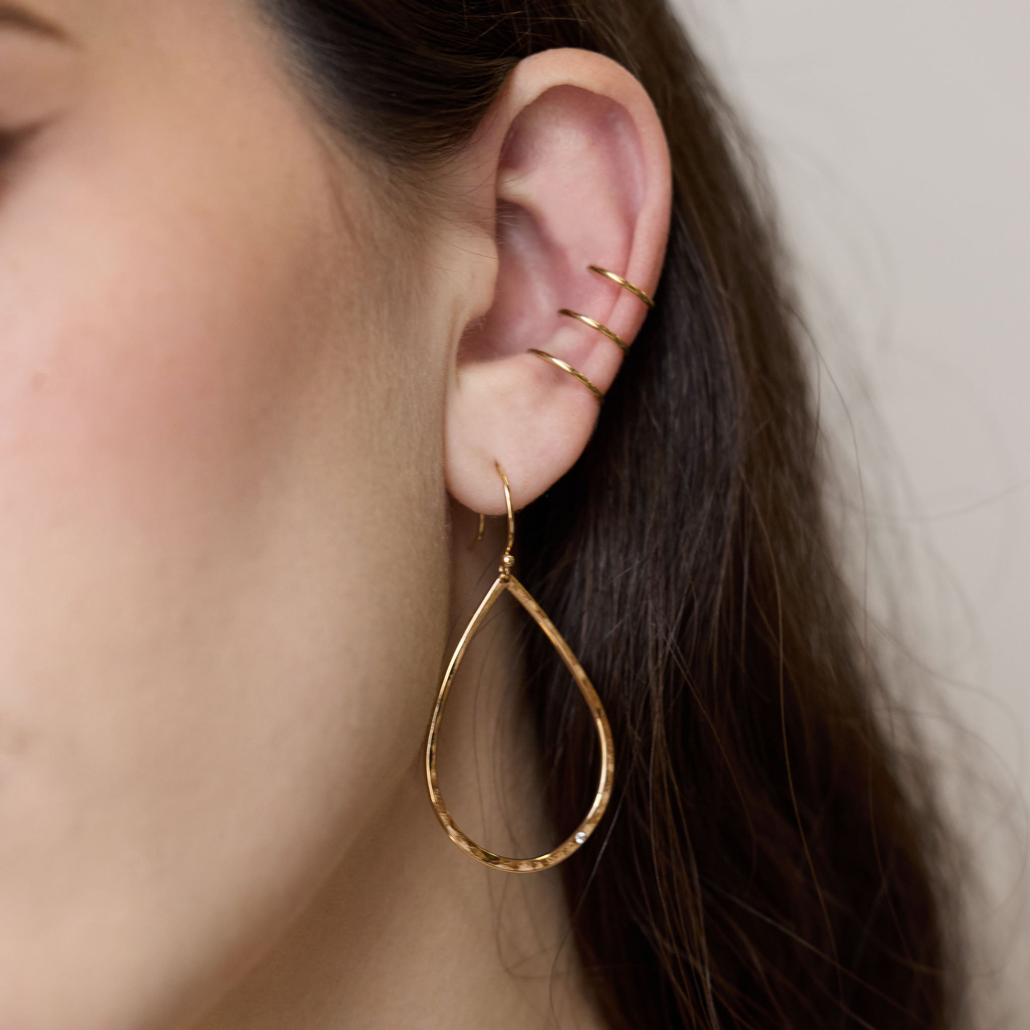 Close up of ear wearing Zoe Chicco 14k gold teardrop hoop earring on a neutral background