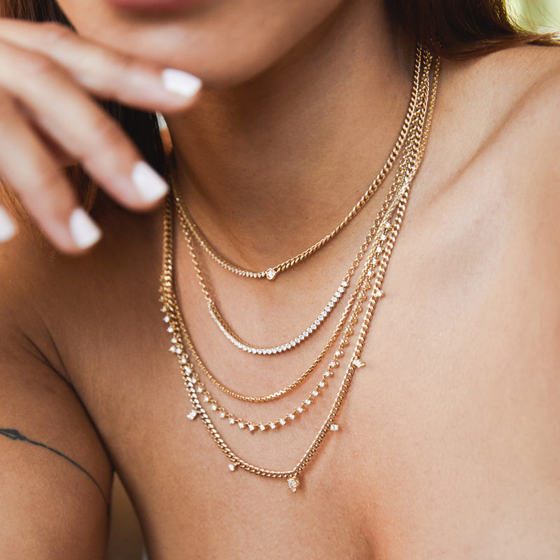 an angled view of a woman wearing a Zoë Chicco 14k Gold Small Box Chain Necklace layered with four diamond necklaces