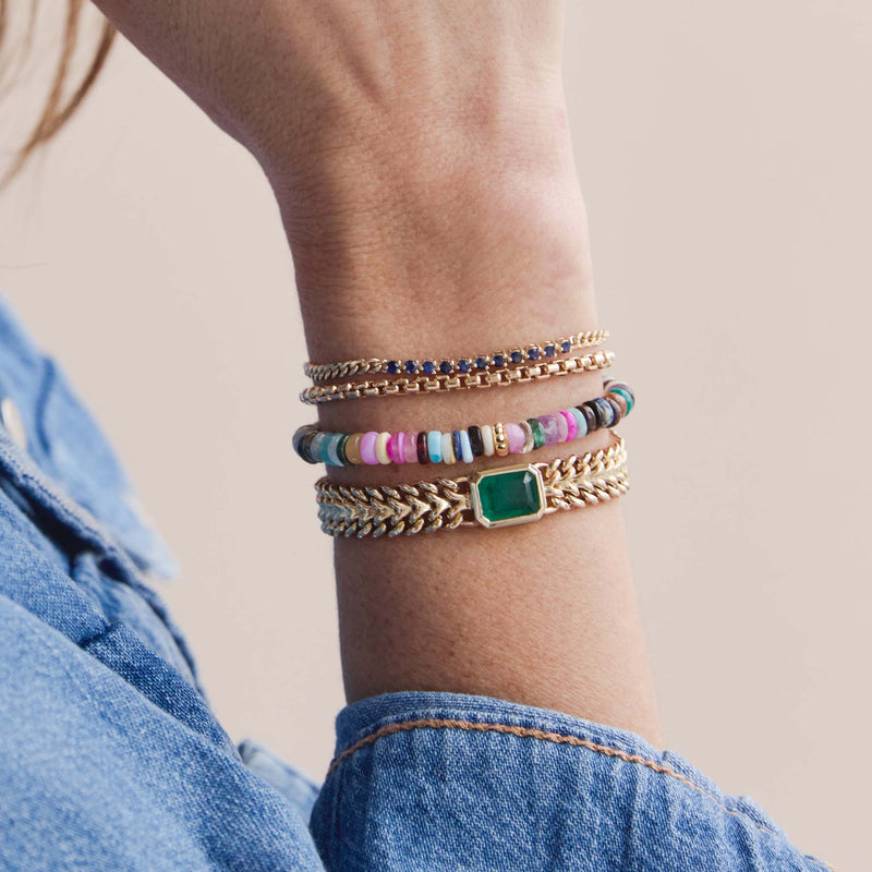 woman in a denim shirt wearing a Zoë Chicco 14k Beaded Gold & Mixed Dark Gemstone Rondelle Bead Bracelet stacked with a one of a kind Emerald cut Emerald Curb Chain Bracelet, Large Box Chain Bracelet, and a Blue Sapphire Tennis Segment Curb Chain Bracelet