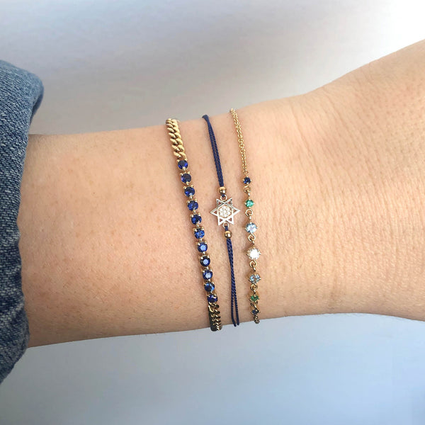 woman wearing a Zoë Chicco 14k Gold Midi Bitty Pavé Diamond Star of David Silk Bracelet stacked with an Ombre Blue Gemstone Bracelet and a Blue Sapphire Tennis Segment Small Curb Chain Bracelet