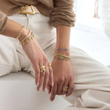 Close up of hands wearing Zoe Chicco 14k gold and colored gemstone rings and bracelets on a light background
