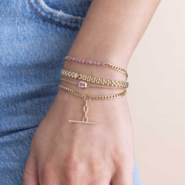 woman's wrist wearing a Zoë Chicco 14k Gold Princess Diamond Small Panther Chain Bracelet layered with a Pink Sapphire Tennis Segment Curb Chain Bracelet, Emerald Cut Pink Sapphire XS Curb Chain Bracelet, and a Pavé Diamond Toggle Bracelet