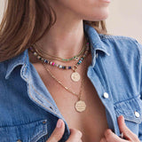 woman in a denim shirt wearing a Zoë Chicco 14k Gold Small Curb Chain Marquise Blue Sapphire Halo Necklace layered with a 14k Gold & Emerald Tennis Segment Curb Chain necklace and a Mixed Dark Gemstone Round Enhancer Necklace with a Diamond Evil Eye Medium Sunbeam Medallion Charm and a Medium Paperclip Rolo Chain Necklace with a Large "Kindness is the signature of the strong" Octagon Mantra Charm Pendant