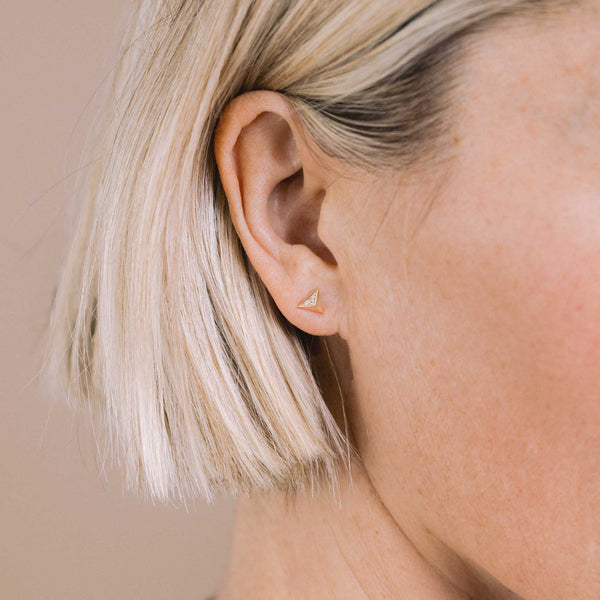 close up of a blonde woman's ear against a beige background wearing a single Zoë Chicco 14k Gold Pavé Diamond Triangle Pyramid Stud Earring