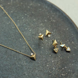a pair of Zoë Chicco 14k Gold Triangle Pyramid & Trillion Diamond Bezel Drop Earrings laying flat on a dark gray marble tray