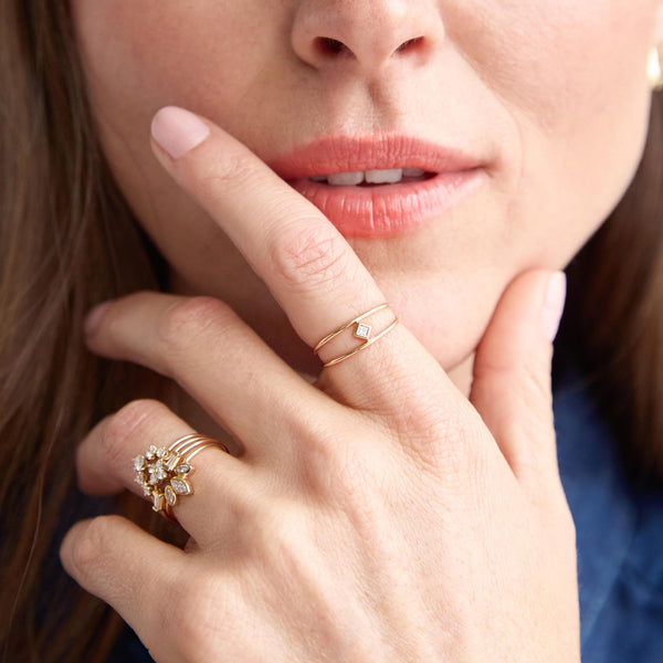 woman resting her hand on her chin wearing a Zoë Chicco 14k Gold Princess Diamond Double Band Ring on her index finger and multiple diamond rings on her ring finger