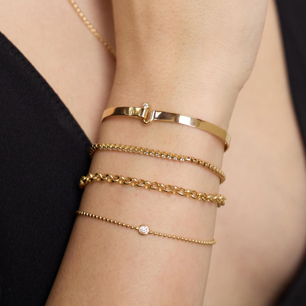 Close up of a person's wrist wearing Zoe Chicco 14k gold chain and diamond bracelets on a blurred backgroud