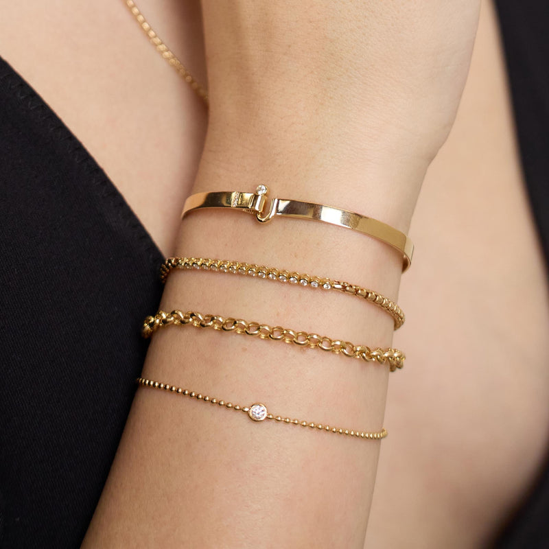 Close up of a person's wrist wearing Zoe Chicco 14k gold chain and diamond bracelets on a blurred backgroud